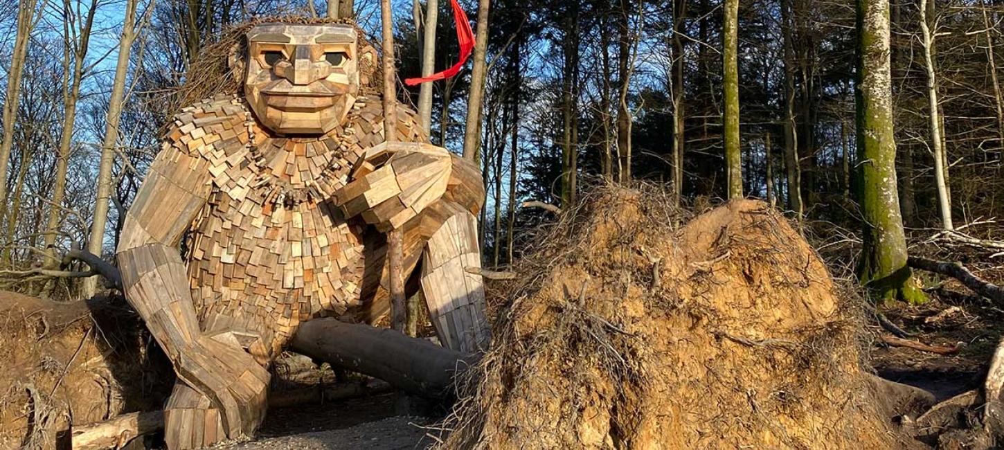 Trold af genbrugstræ sidder i skov med flag